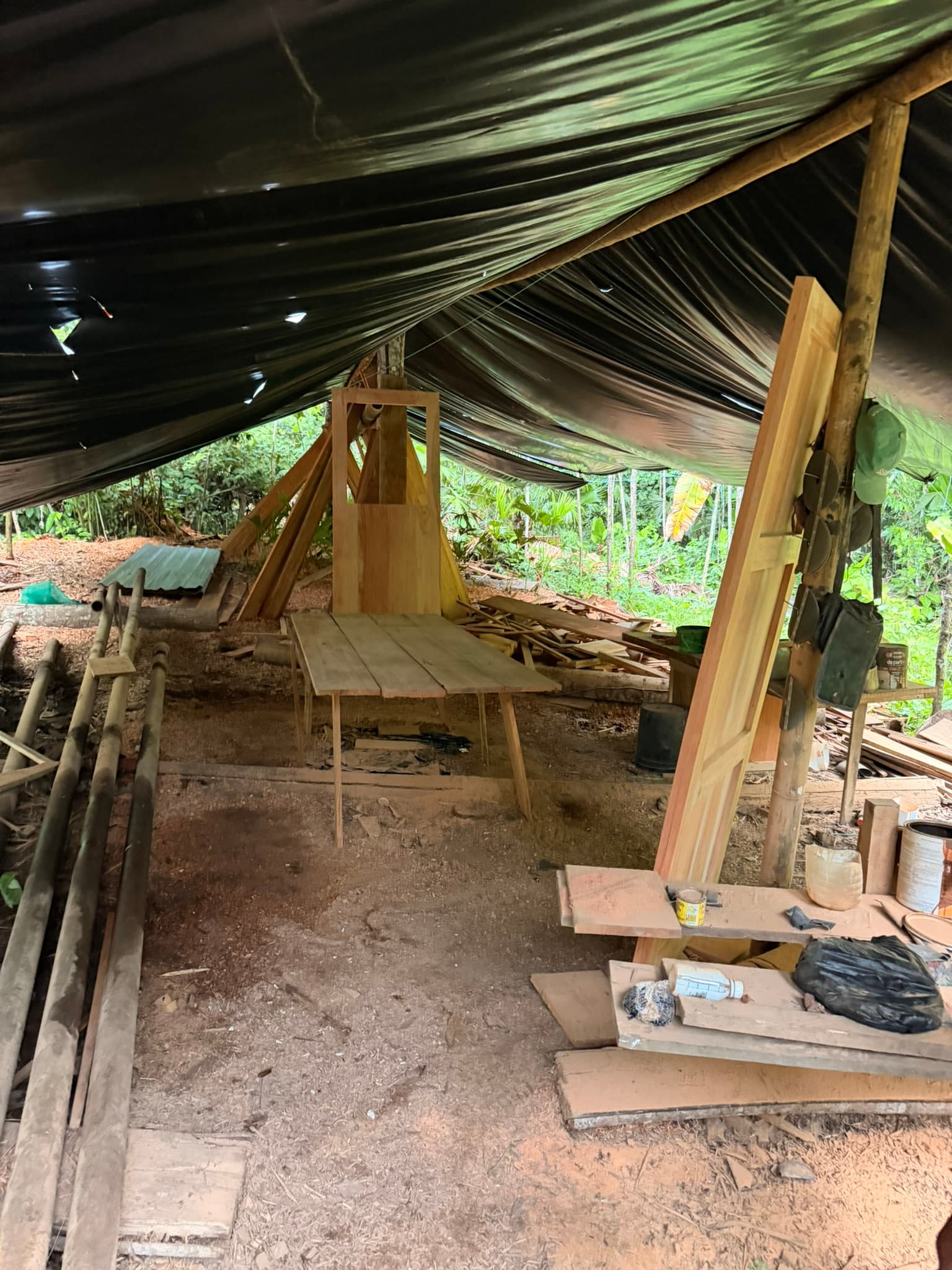 Taller de carpintería al aire libre bajo una lona negra en la selva del Yasuní, Ecuador.
